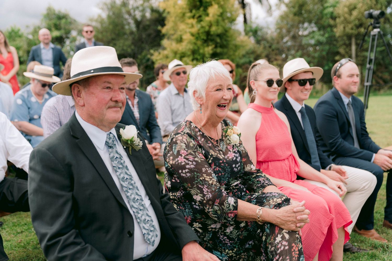 Wedding guests seated outdoors enjoy the ceremony on a sunny day.