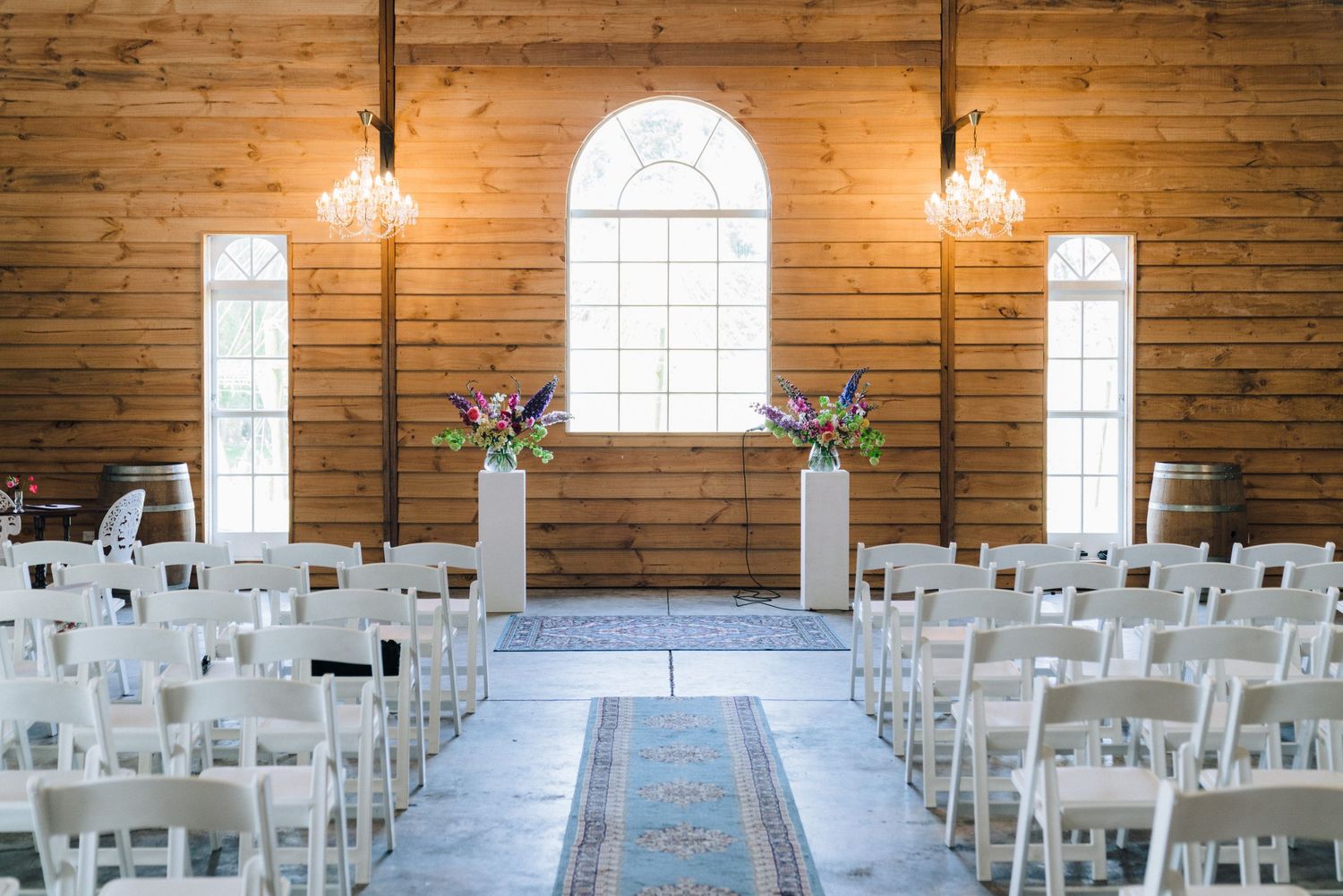 Elegant rustic wedding chapel interior with wooden walls, arched windows, and rows of white chairs illuminated by warm lighting.