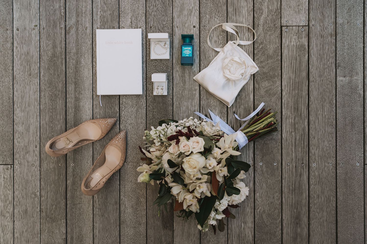 Wedding accessories including white bouquet, ballet flats, paper items, and lantern arranged on rustic wooden floor.