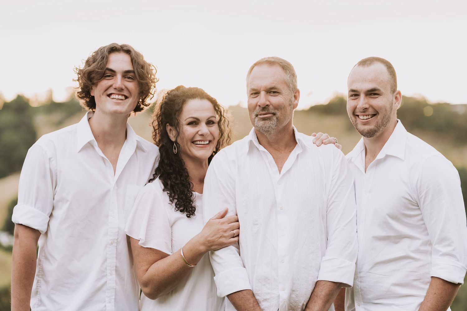 A small group wearing coordinated white casual shirts smiling together outdoors during golden hour.