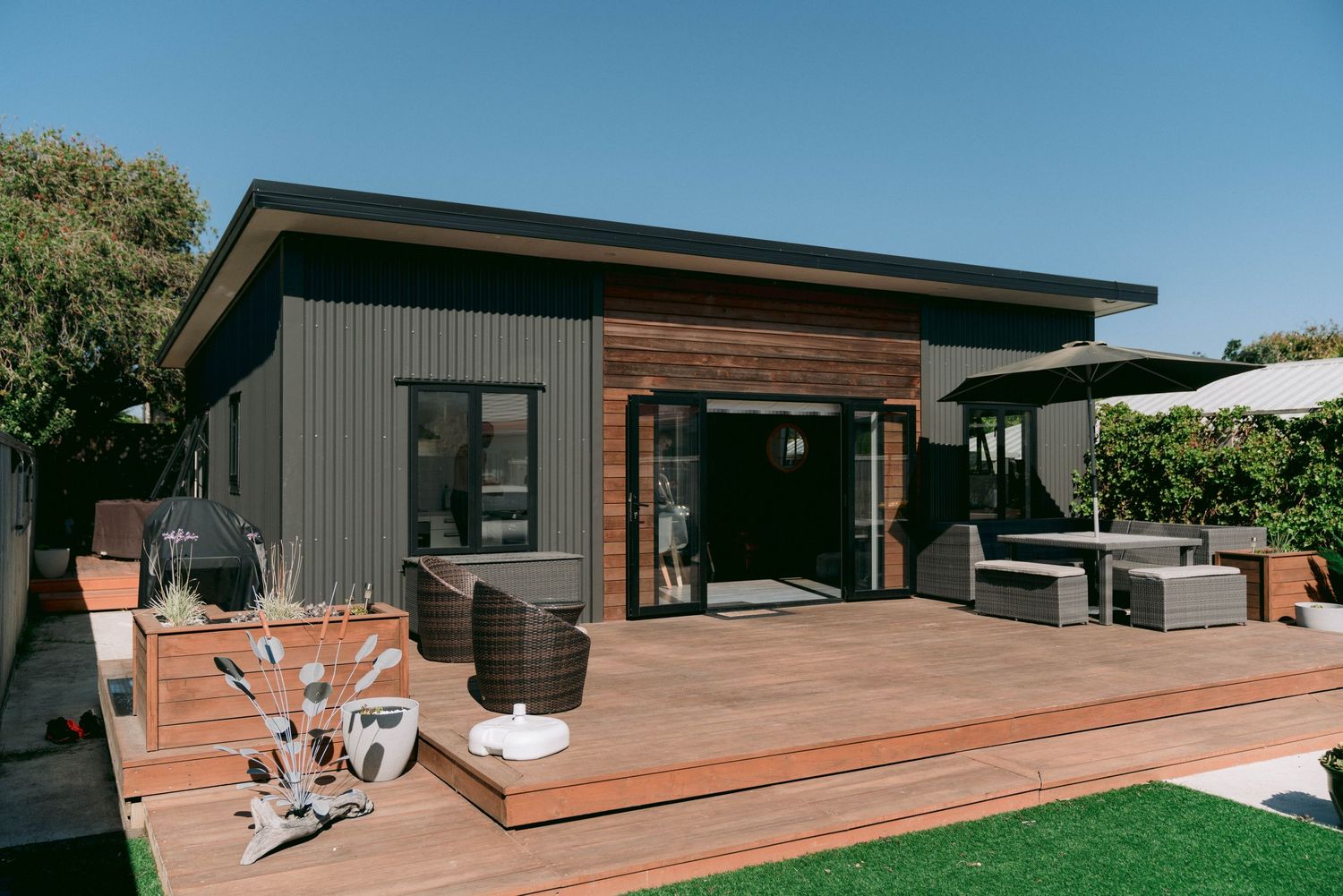 Modern backyard deck features wood planking, gray siding, and contemporary outdoor furniture with lounge seating area.