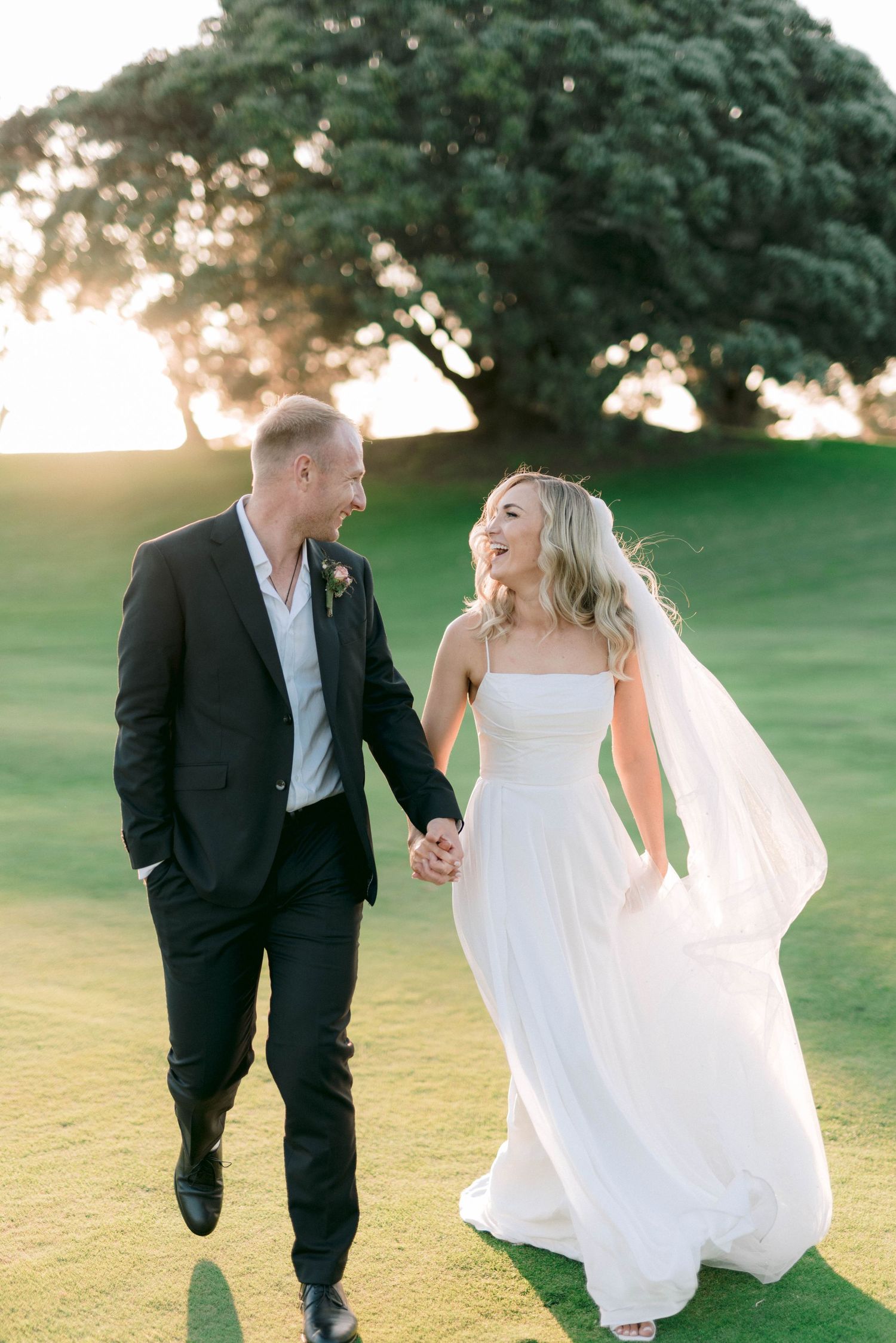 A couple playfully runs together on a lush green golf course during their wedding photoshoot.