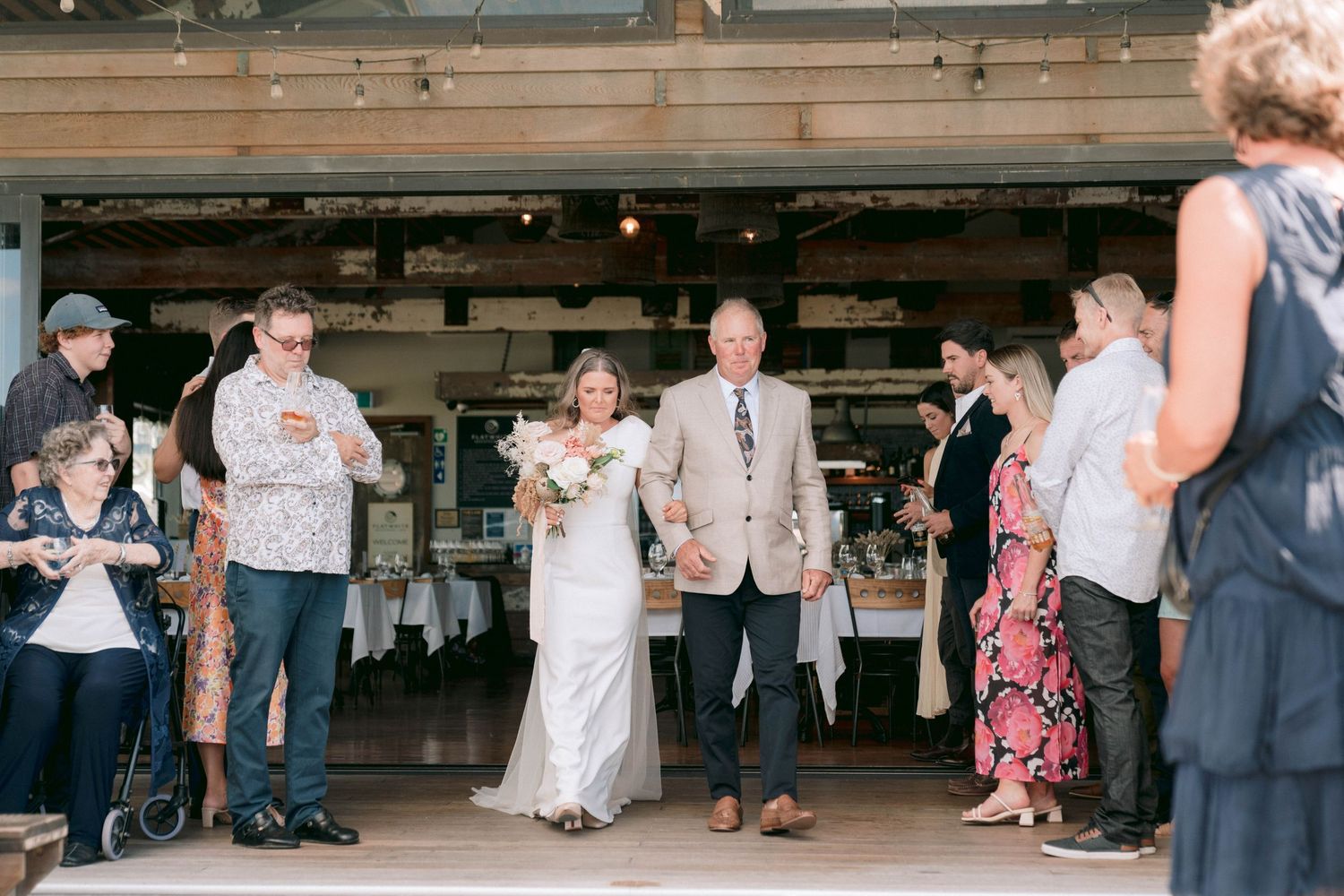 Wedding couple makes their entrance into the reception venue as guests look on.