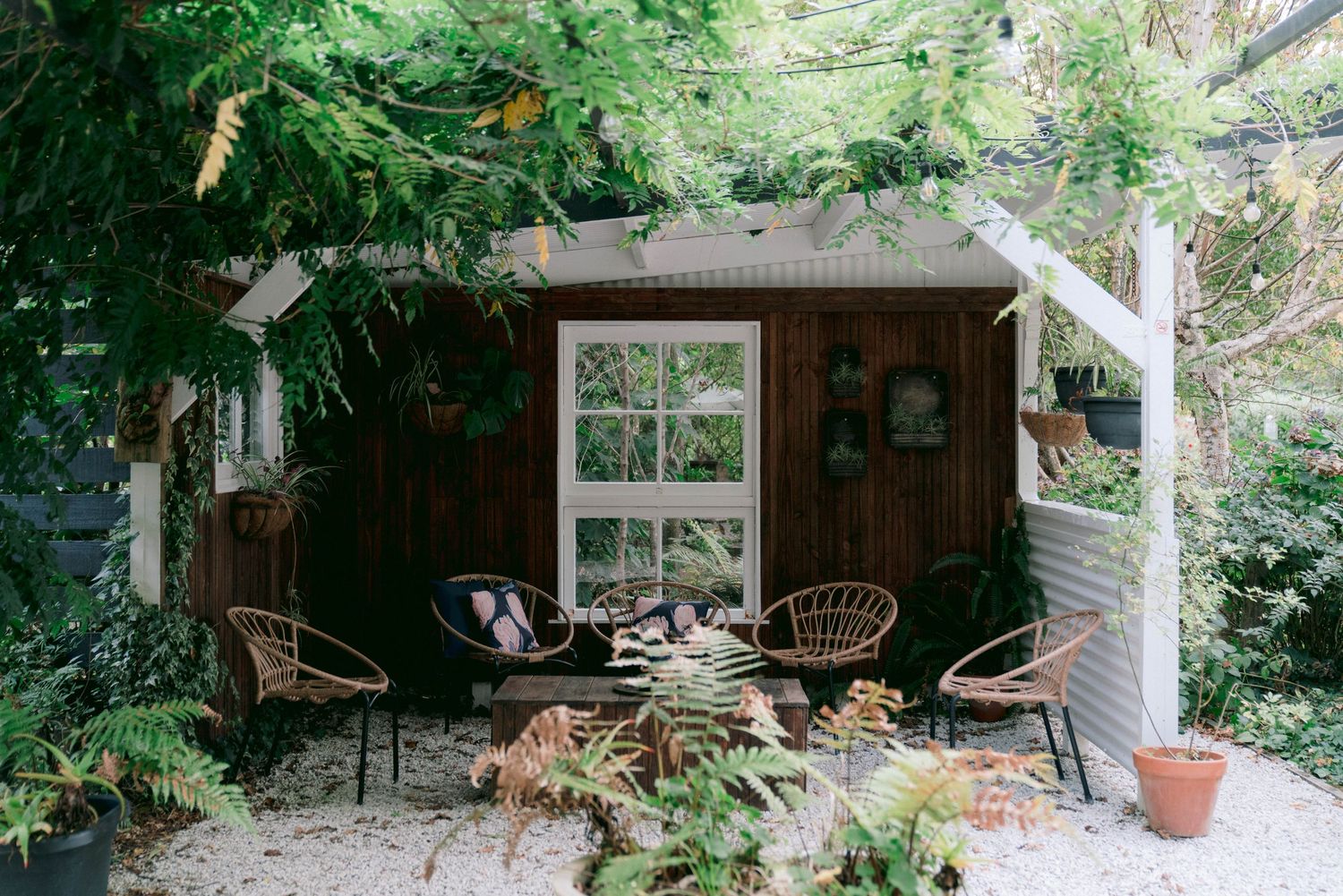 Rustic wooden shed with patio furniture surrounded by lush garden foliage.