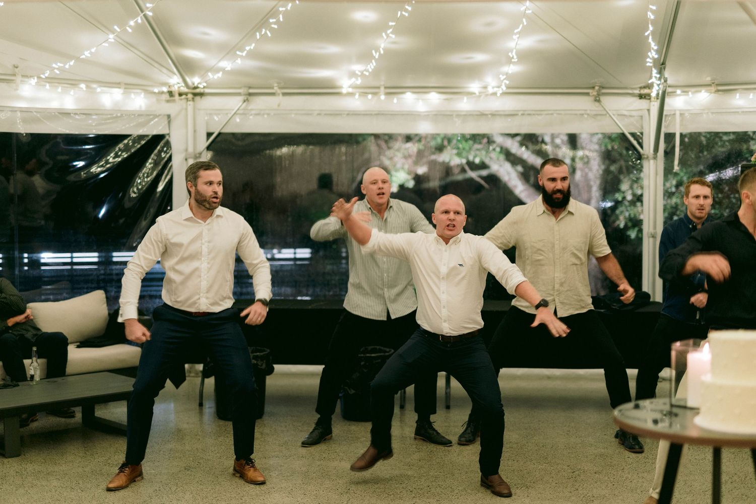 Group of celebrants performing synchronized leg kicks in a dance line at a wedding reception.