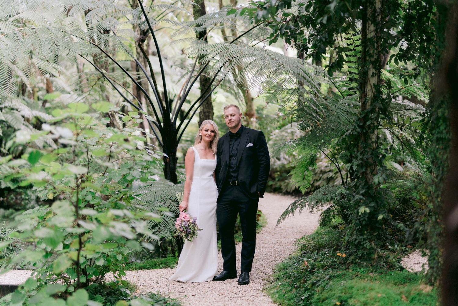 A couple poses on a winding garden path surrounded by verdant foliage.