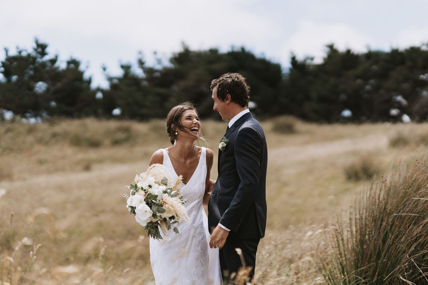 A couple in wedding attire walks together through a scenic outdoor field during their special day.