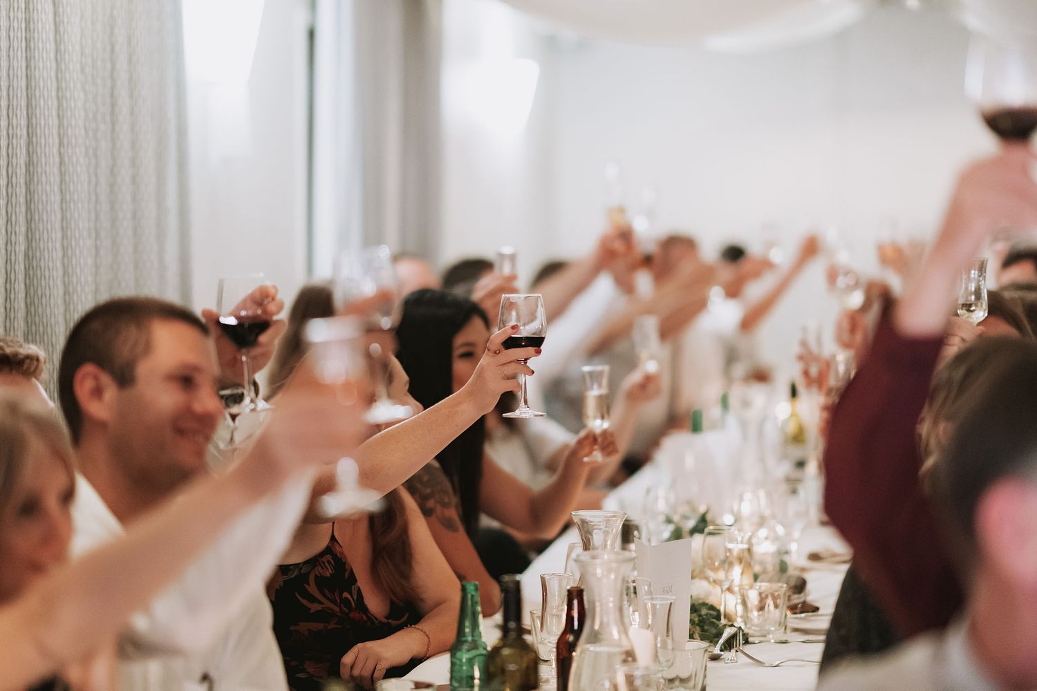Wedding reception guests raise their glasses in a toast at elegant table setting during dinner celebration.