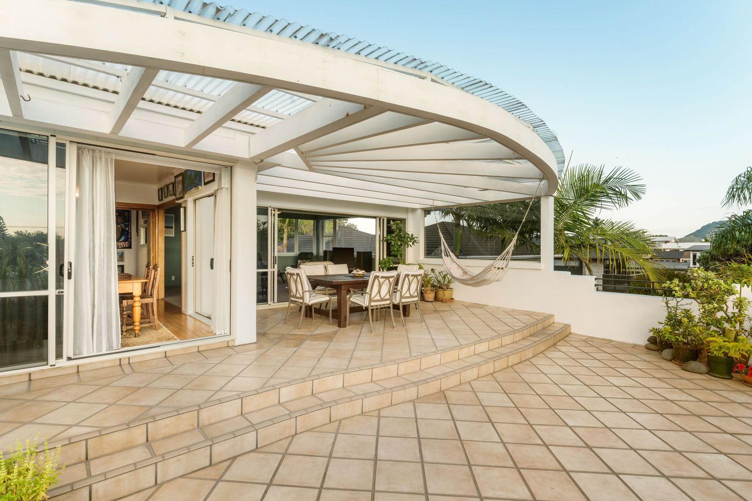 Modern tiled deck with white pillars and tropical landscaping overlooking a scenic outdoor area.