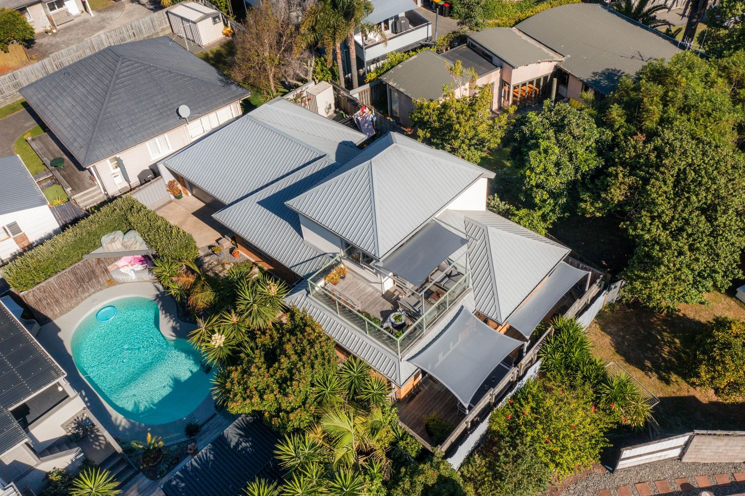 Aerial drone view of modern suburban homes with swimming pools and lush landscaping in a residential neighborhood.