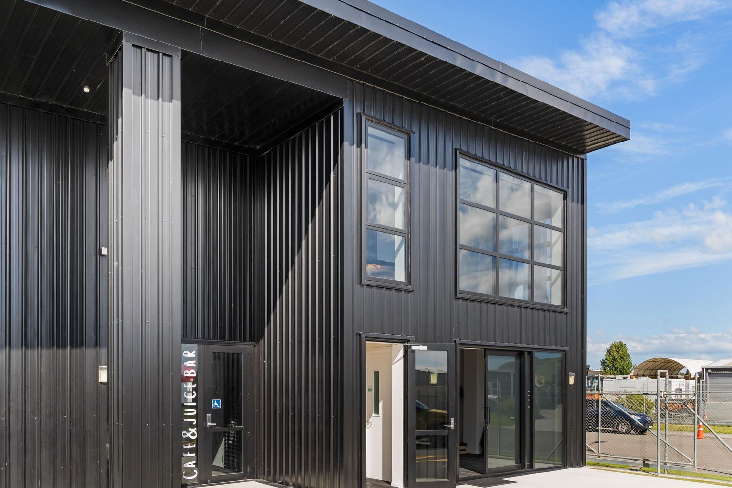 Modern black exterior commercial building with large windows and vertical siding under blue sky.