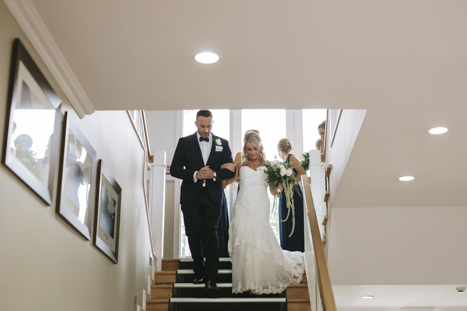 Wedding party carrying gifts and shopping bags down a hallway in formal attire.