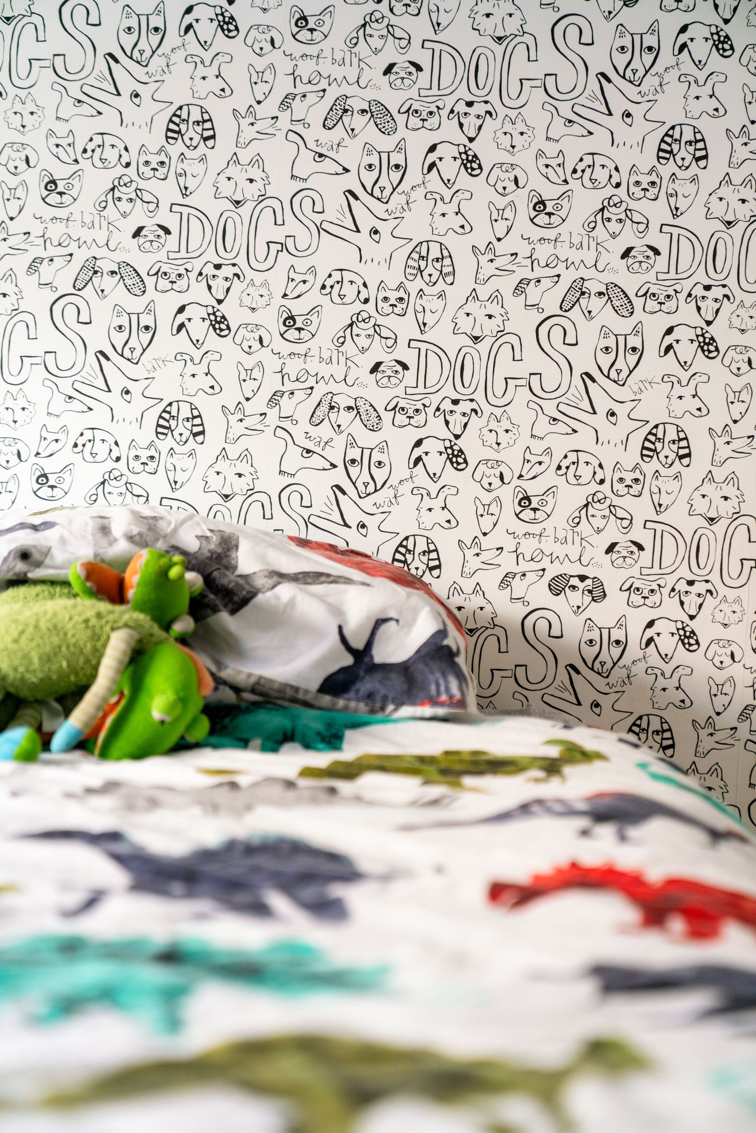 Multiple views of patterned wallpaper with a black and white dog motif above scattered plush toys on bedding.