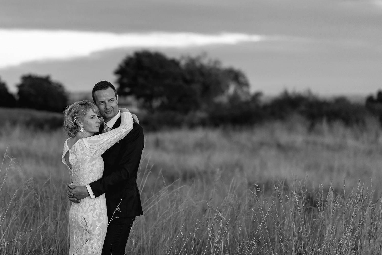 A romantic black and white photo of a couple embracing in a serene meadow at dusk.