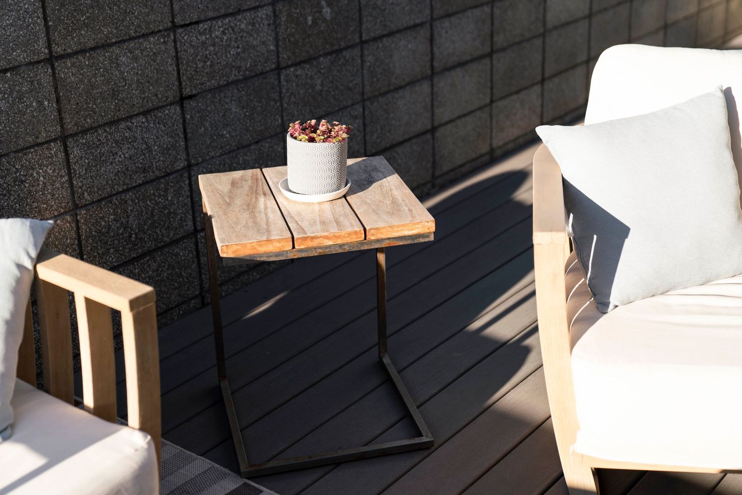 Minimalist outdoor seating area with wooden side table and white cushioned chairs in sunlight.