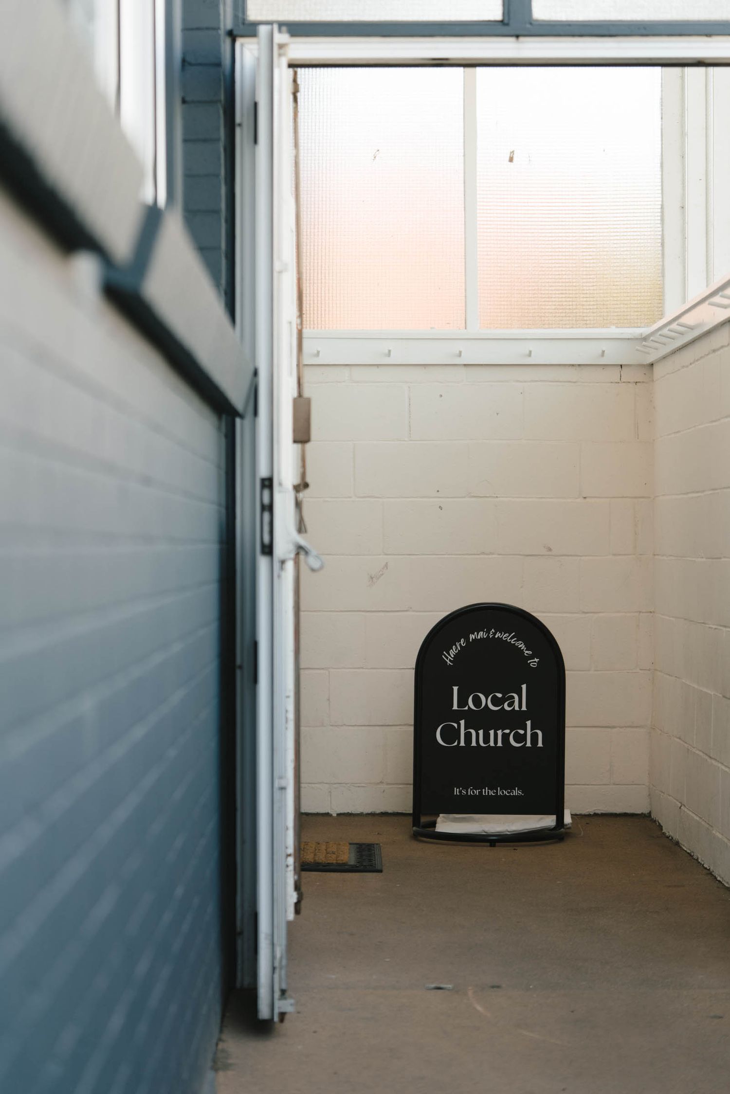 A black sign reading 'Local Church' placed against a white wall in a corner hallway.