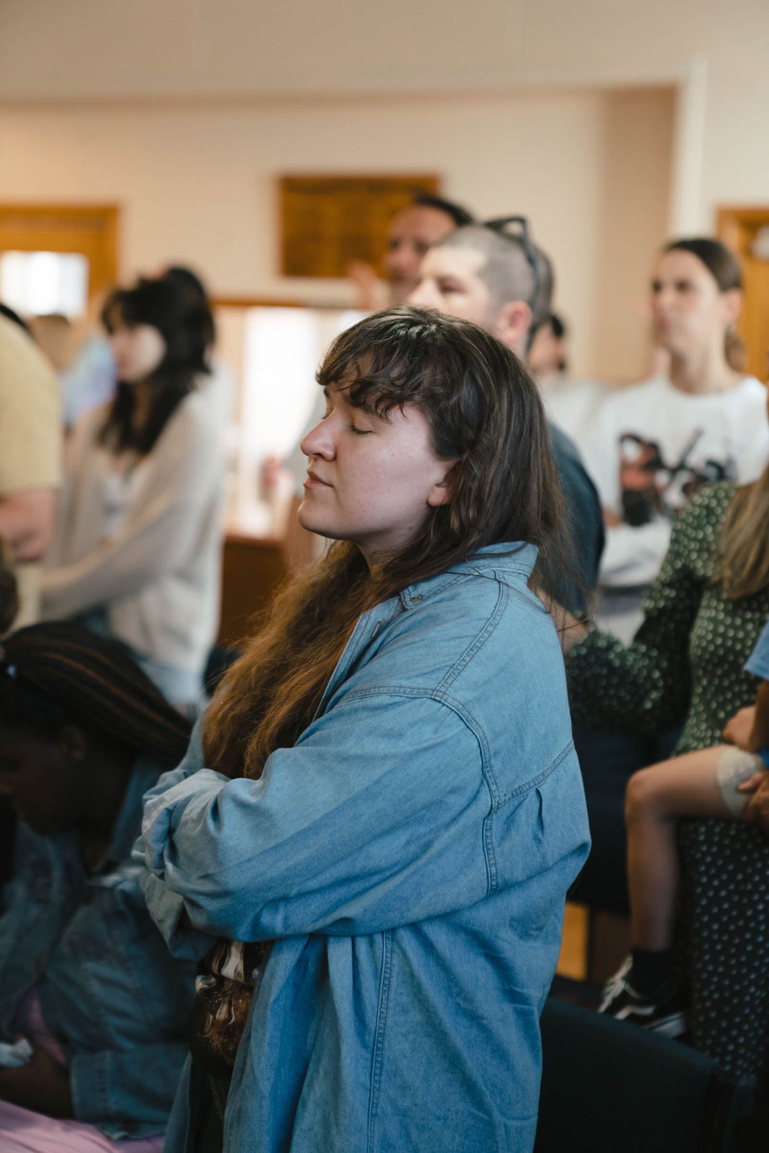 Person wearing denim jacket watching intently in an audience.