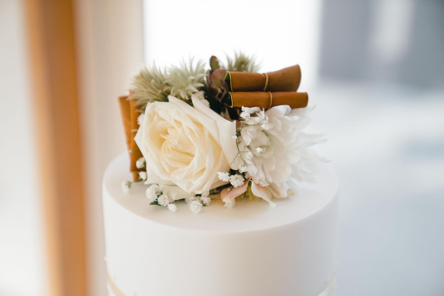 Close-up of white wedding cake topped with cream roses, dried flowers, and cinnamon sticks.