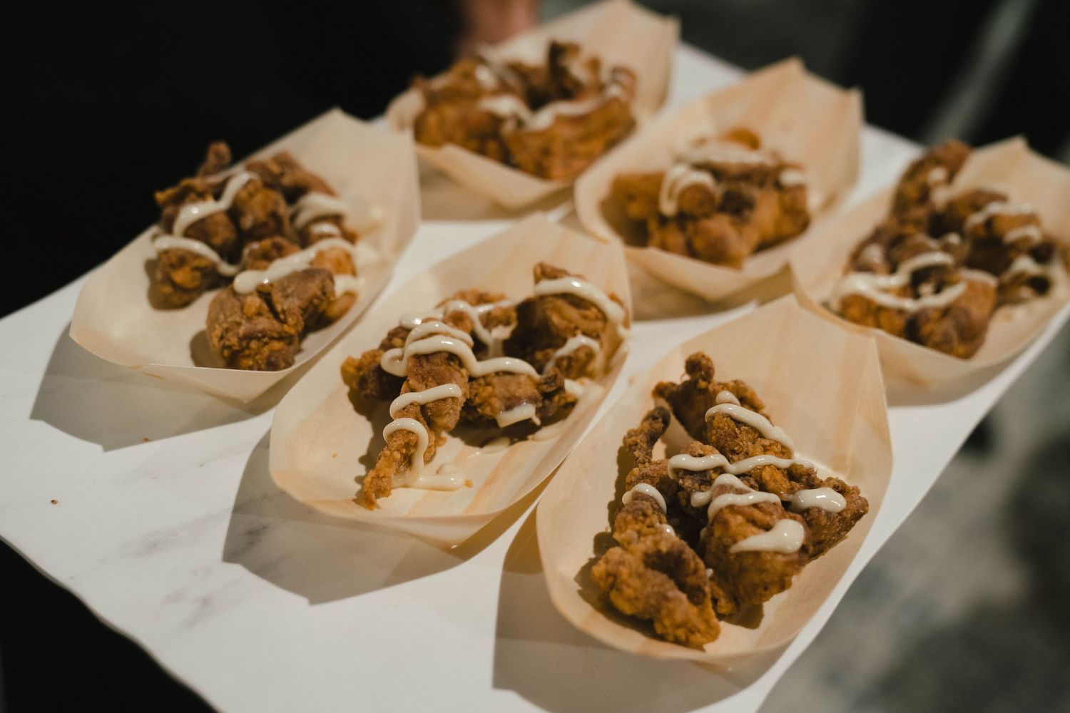 Appetizers served in paper boats on white serving tray at catered event.