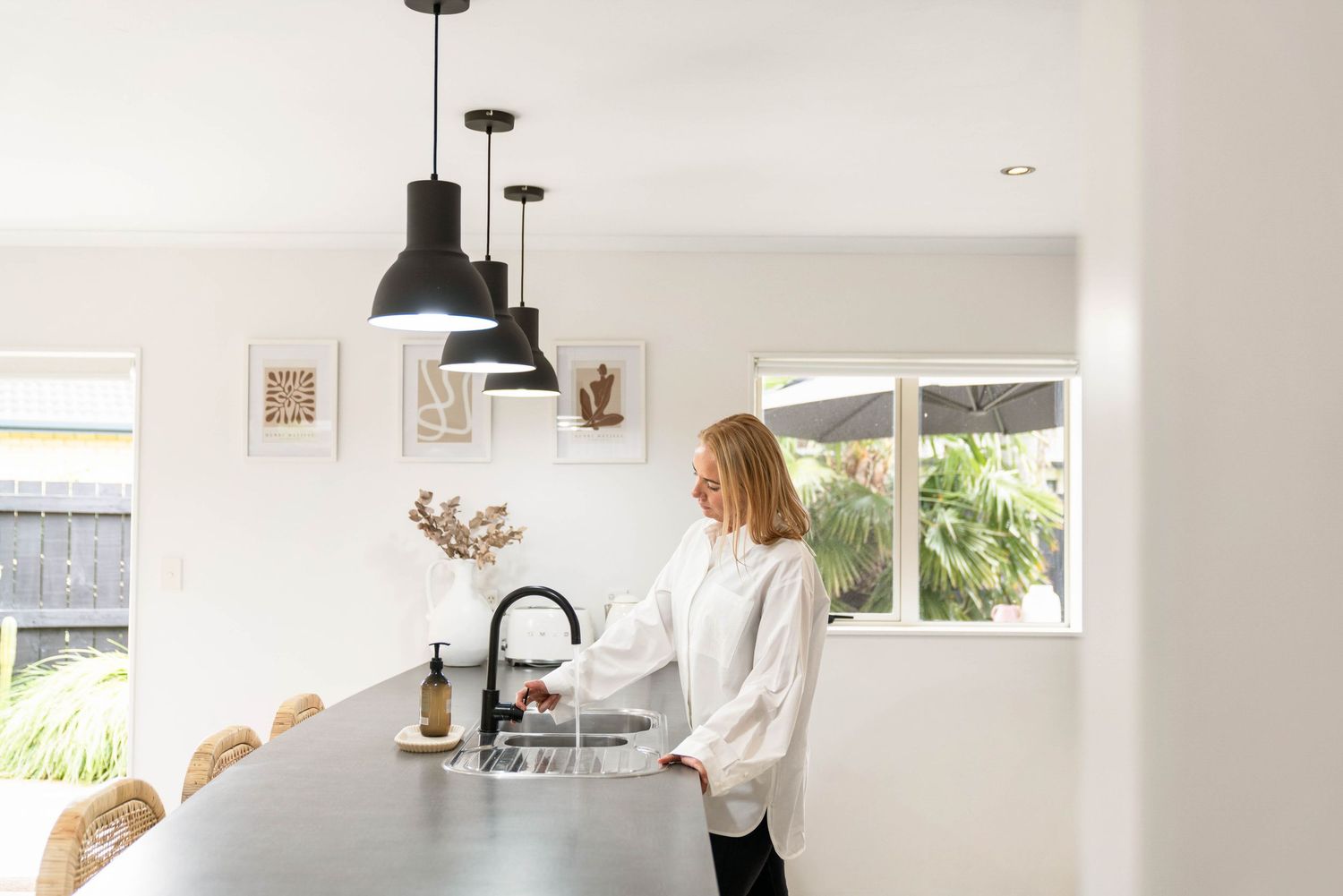 White contemporary kitchen interior with black pendant lights and natural light streaming through windows.