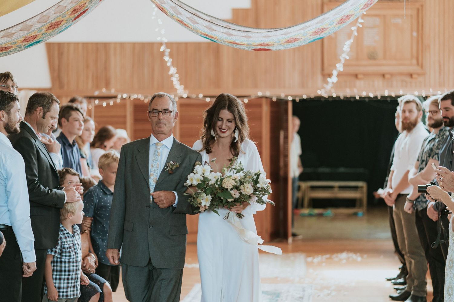 Guests gather in a rustic wooden barn venue decorated with string lights for an elegant wedding celebration.