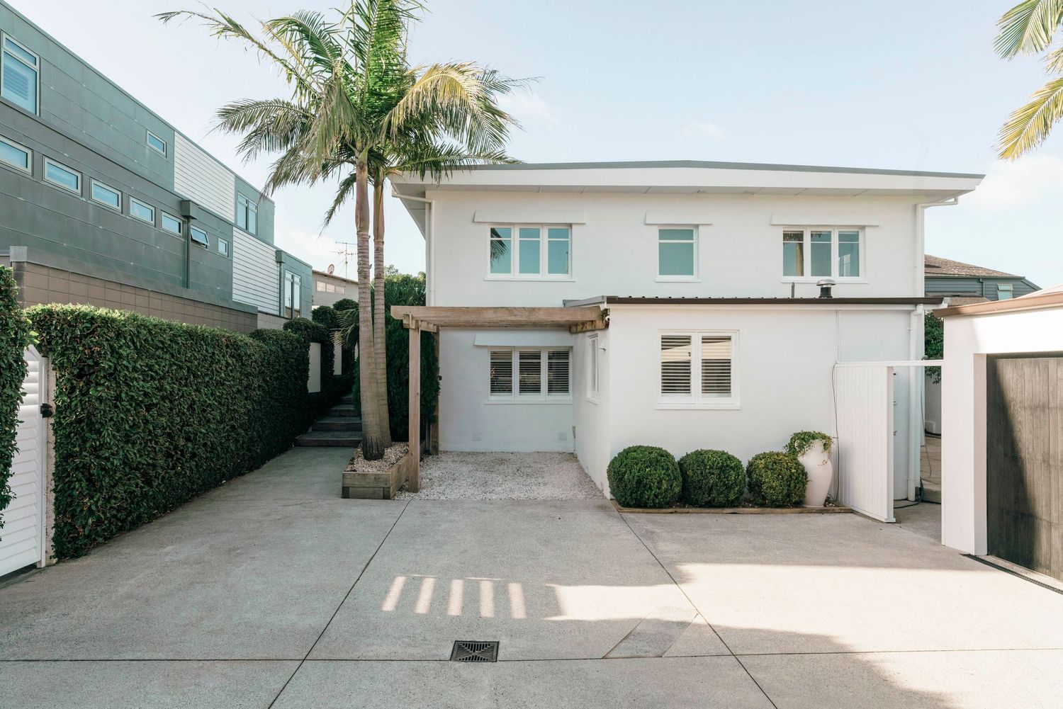 Modern white house exterior with palm trees and a spacious driveway.
