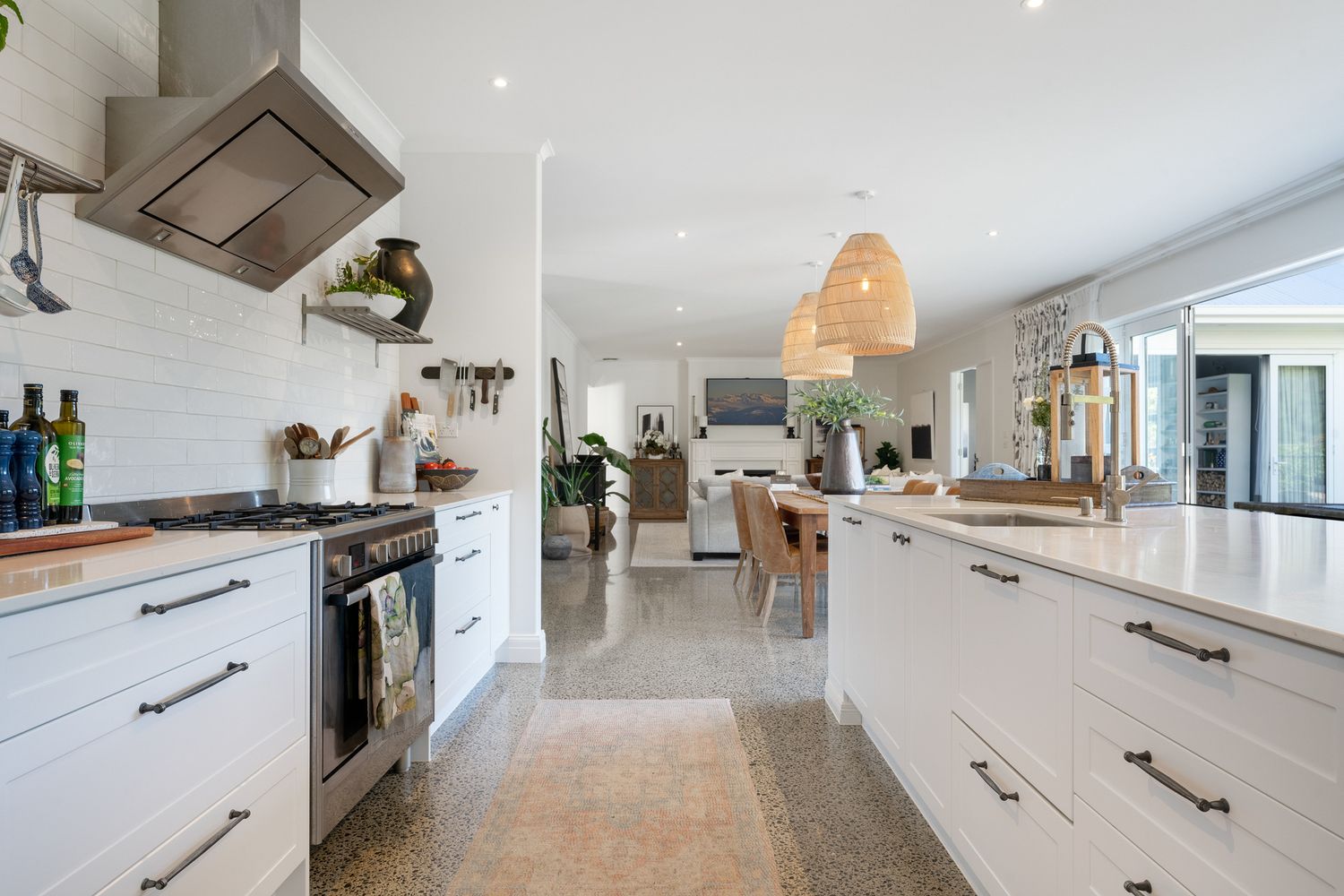 Long galley kitchen with white cabinetry, stainless appliances and rattan pendant lighting.