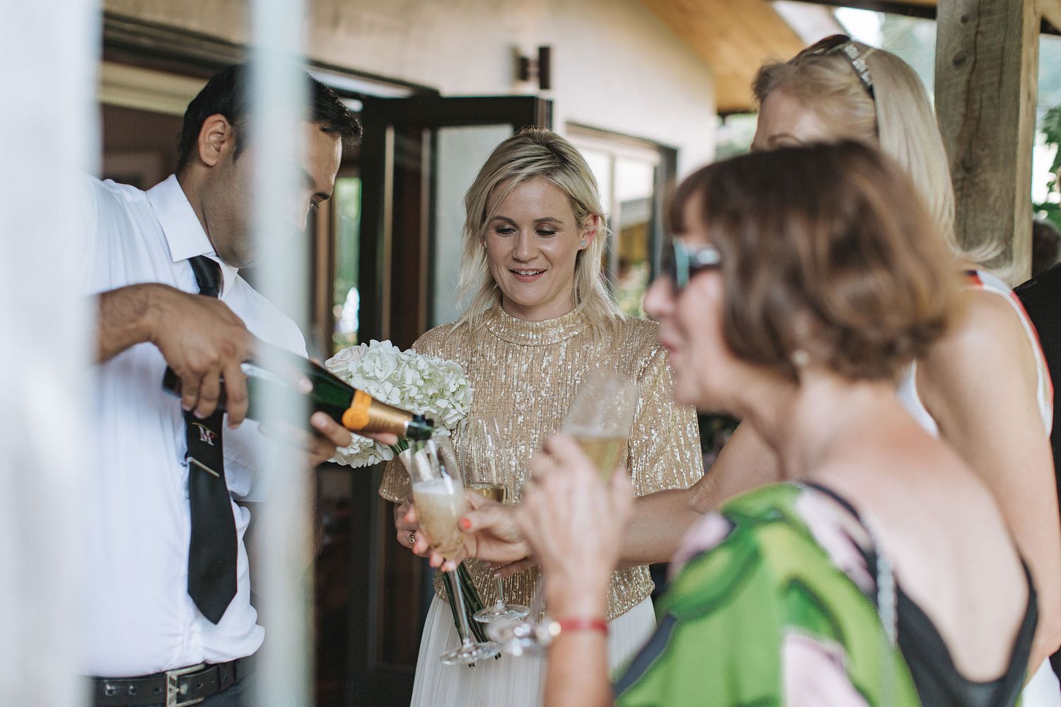 A group of elegantly dressed wedding guests laughing and mingling at an indoor reception area.