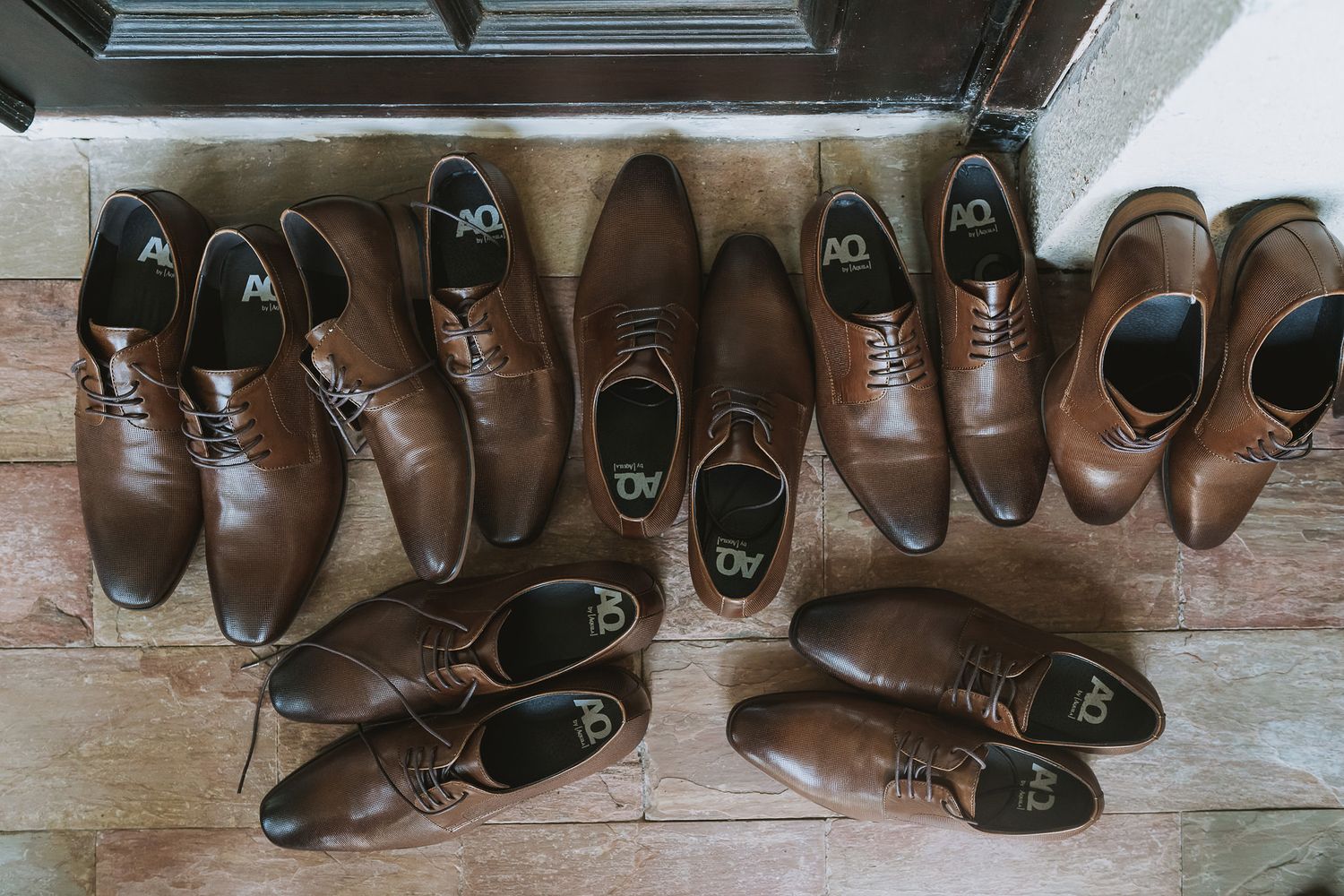 Multiple pairs of brown leather dress shoes arranged in a row on a wooden floor.