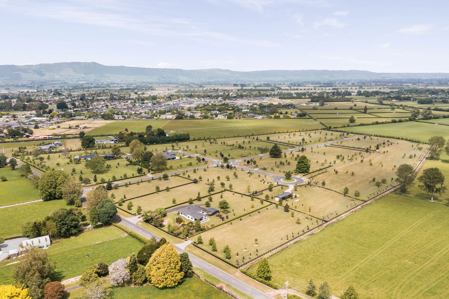 Aerial view of rural countryside with scattered homes, green fields and mountains in the distance.