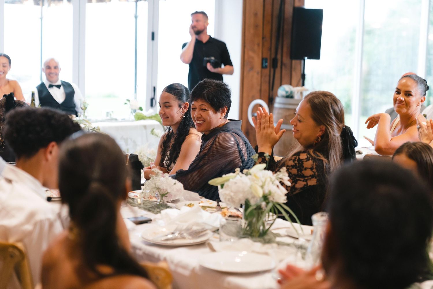 Wedding guests seated at elegant round tables in a bright reception venue during dinner service.