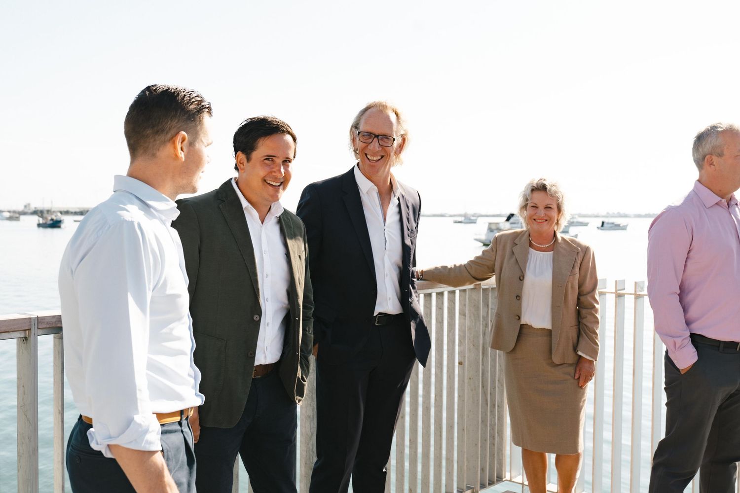 Business professionals engaged in a casual conversation on an outdoor deck with ocean views.