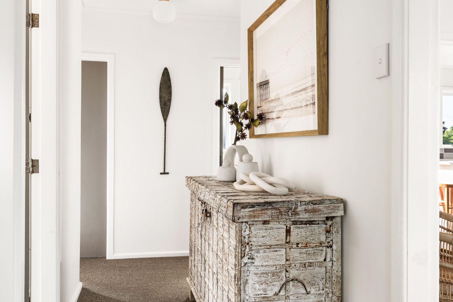 Rustic distressed white console table with mirror and decorative oar in hallway.