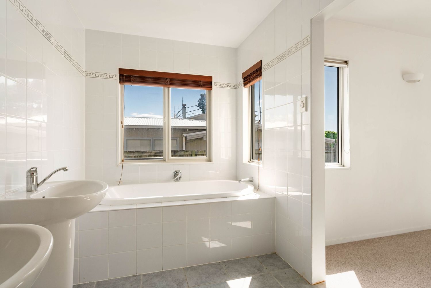 Modern white bathroom with built-in tub, dual sinks and large windows providing natural light.