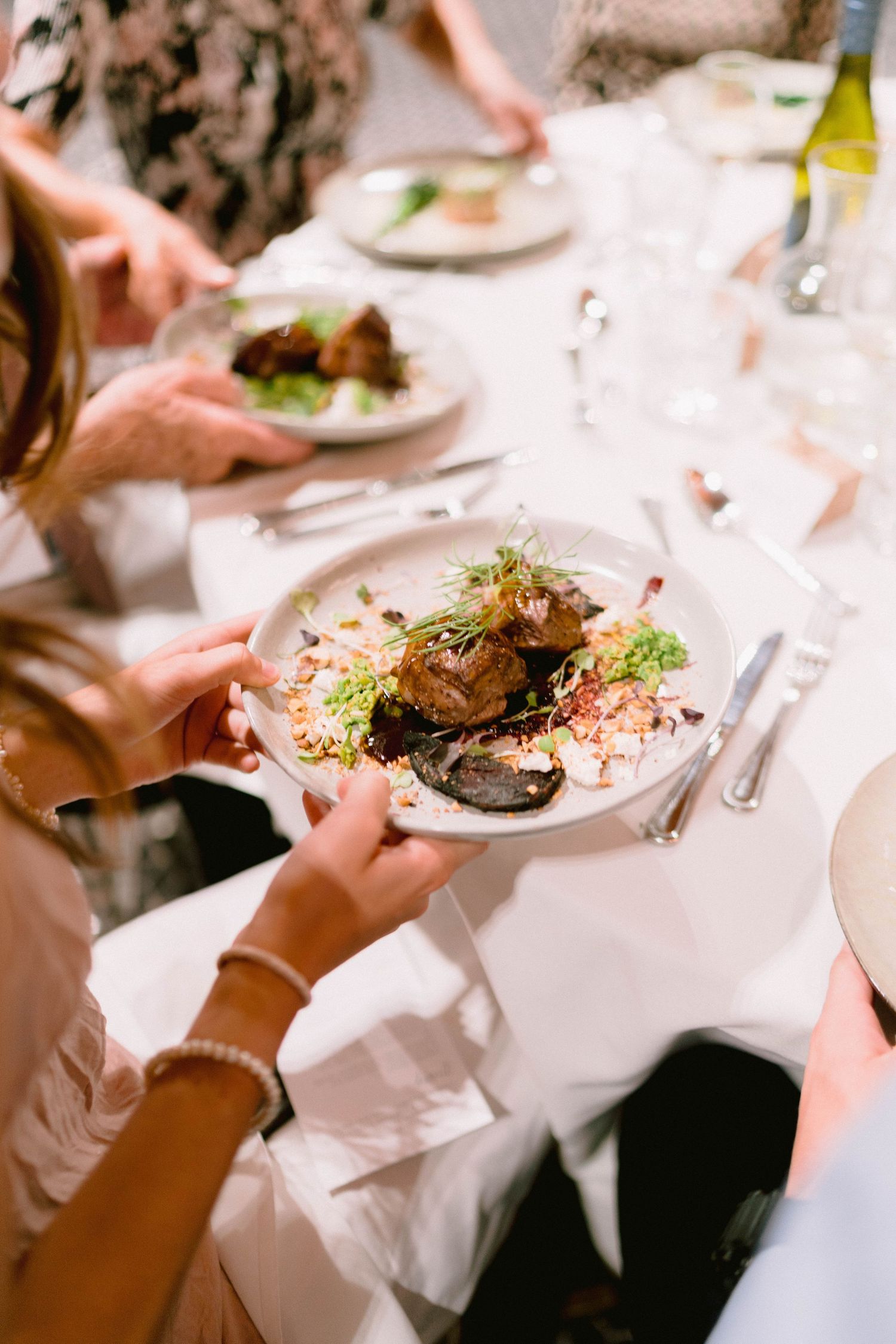 Wedding reception dinner plates with elegant food being served at tables with white linens.