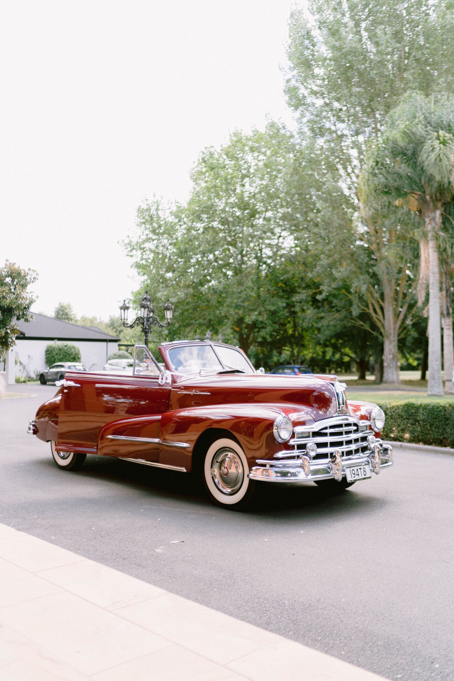 Classic burgundy vintage convertible car parked on a tree-lined street.