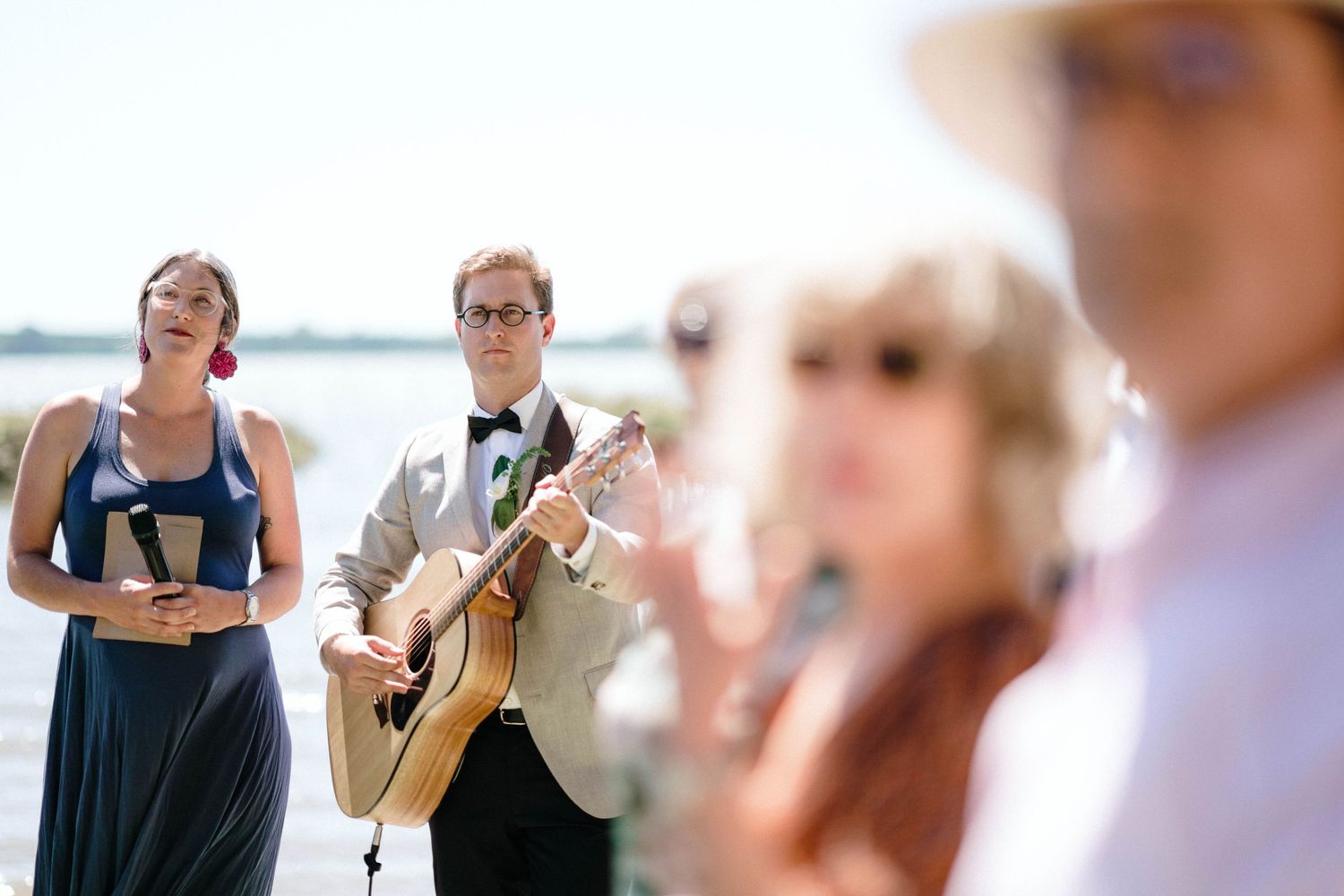 Musicians performing at an outdoor wedding ceremony beside a waterfront setting.