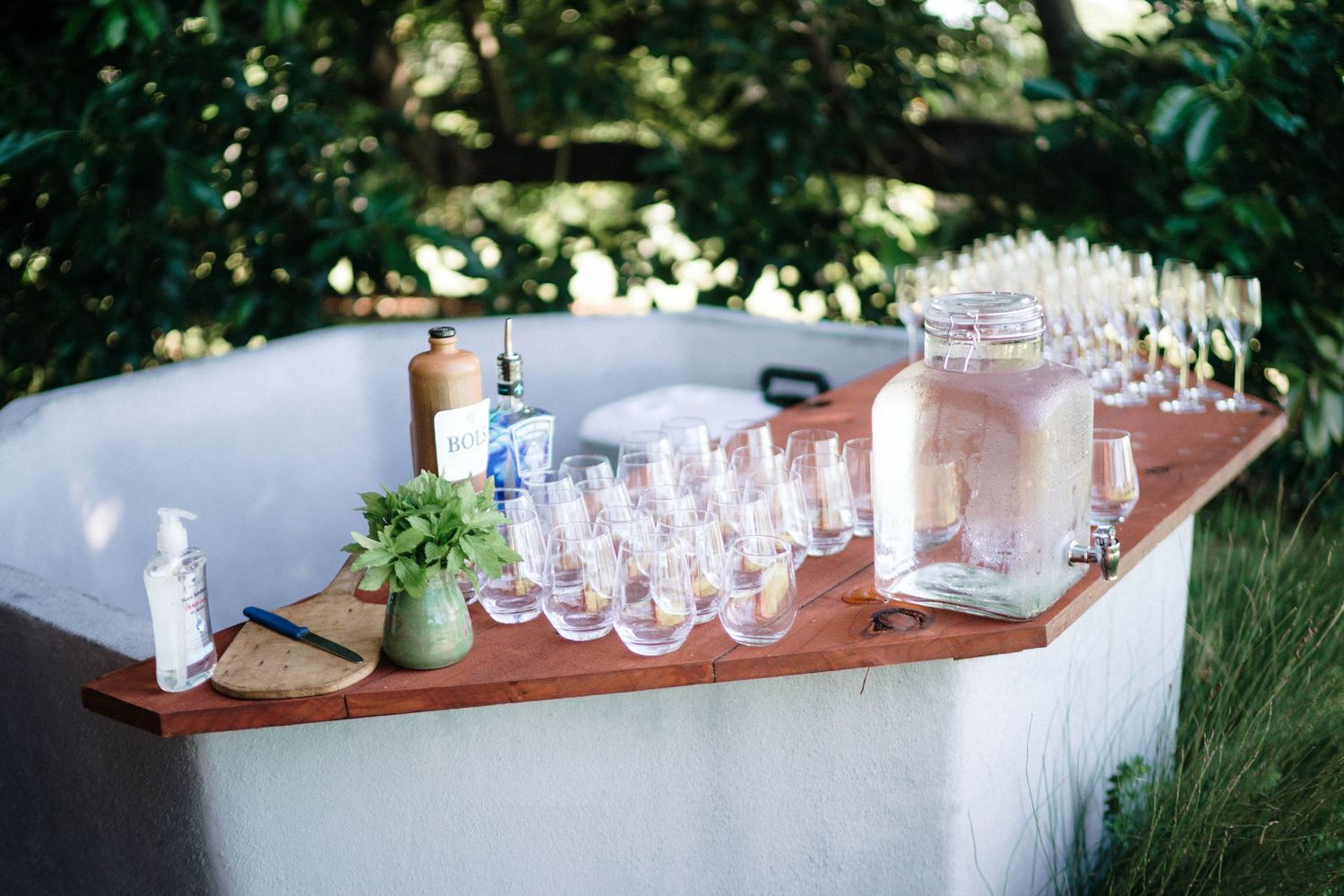 Multiple rows of elegant wine glasses arranged on wooden tables at an outdoor event setup.
