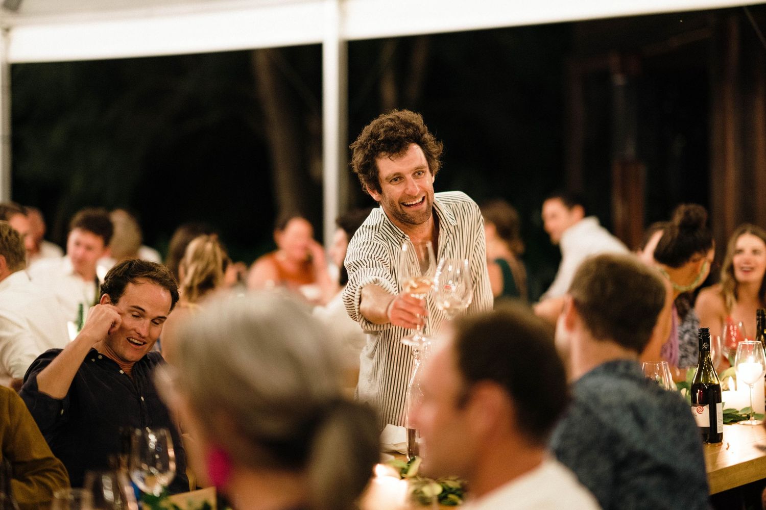 Guests enjoy a candlelit dinner reception at elegant tables in a dimly lit indoor venue.