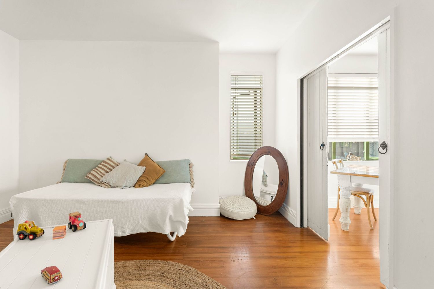 Minimalist white bedroom with hardwood floors, a simple bed, and decorative accents including throw pillows.