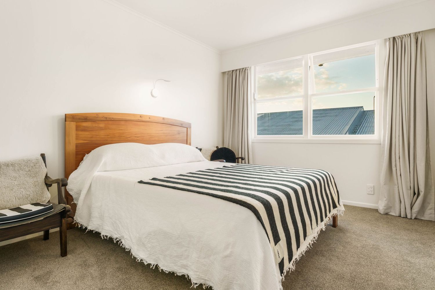 Bright bedroom with crisp white bedding and striped pillows featuring natural light through large windows.