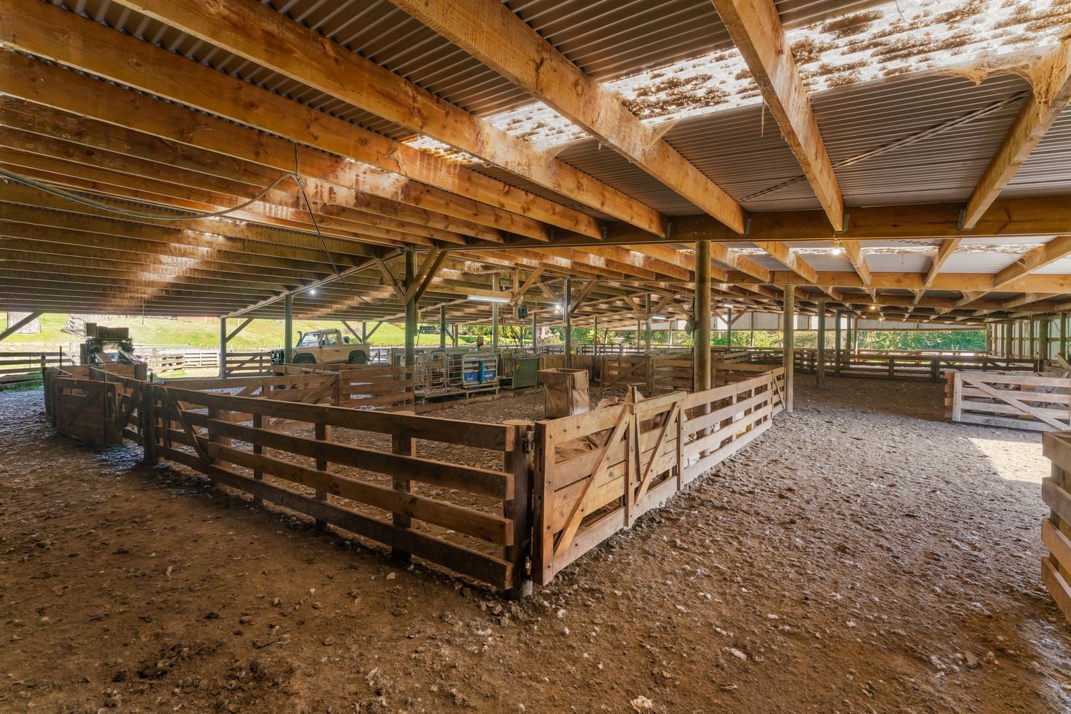 Large covered horse arena with wooden fencing and dirt floor under exposed wooden beams.