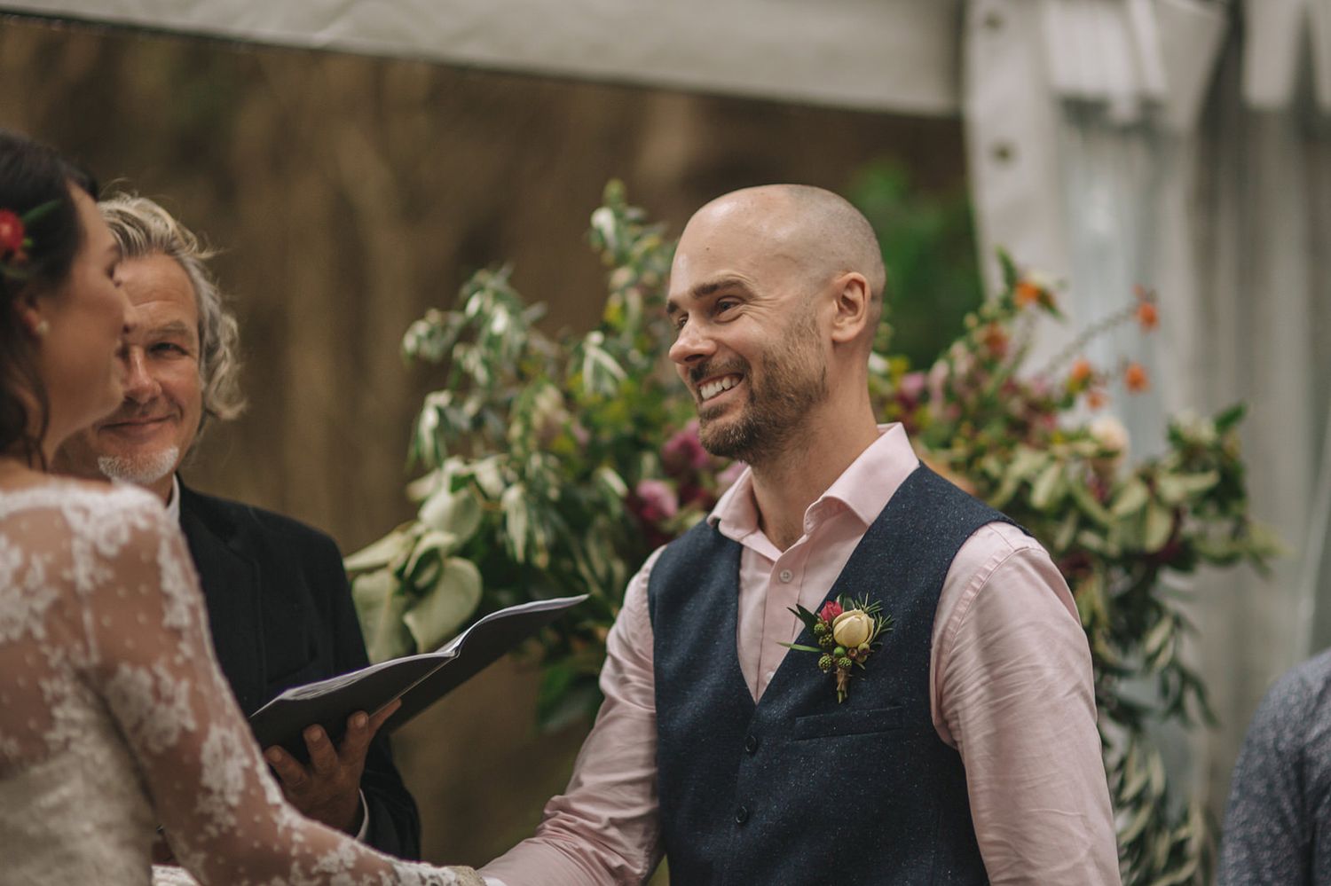A joyful outdoor wedding ceremony takes place with guests and an officiant gathered amongst floral decorations.