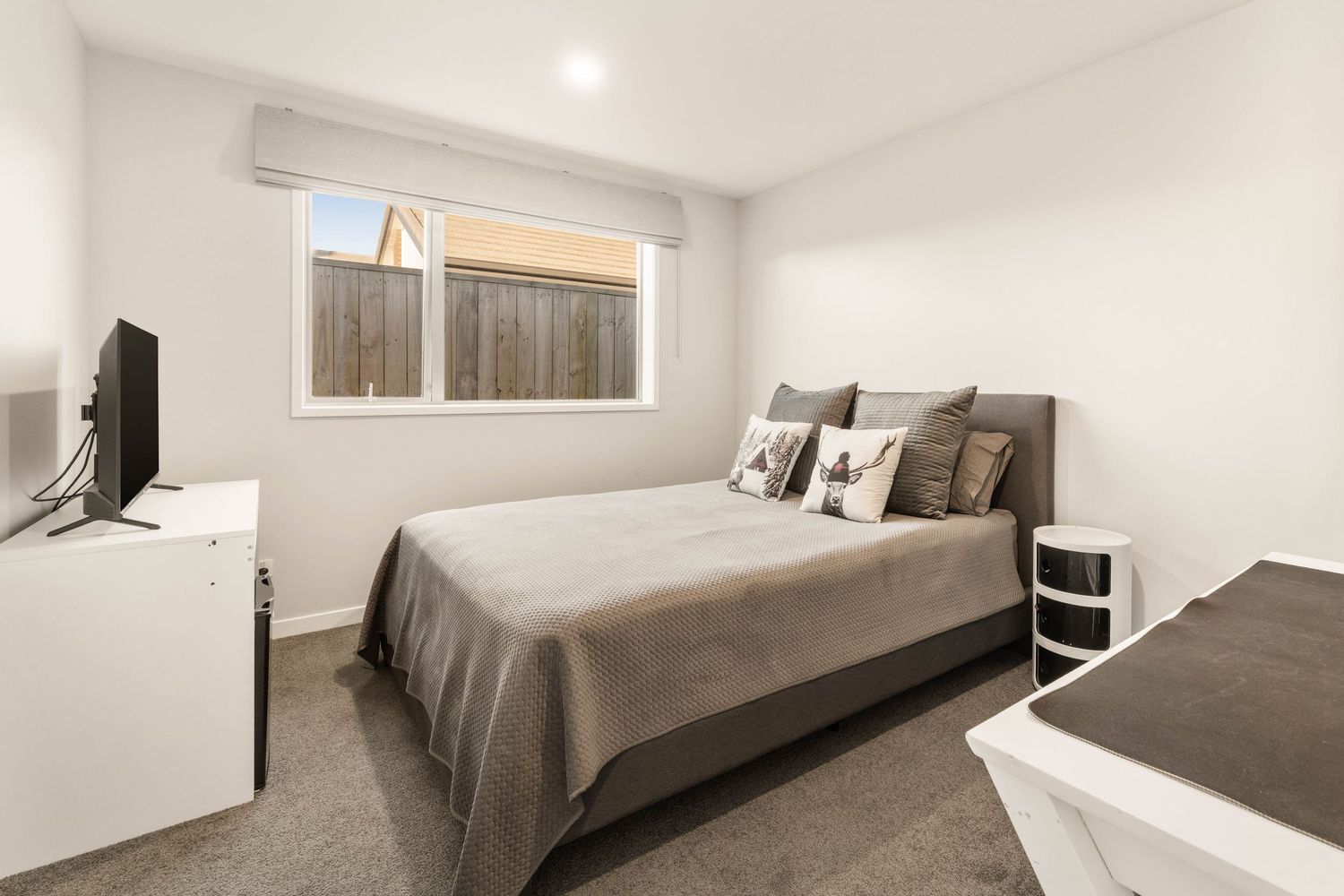 Minimalist bedroom with gray bedding, wall-mounted TV, and white furniture.