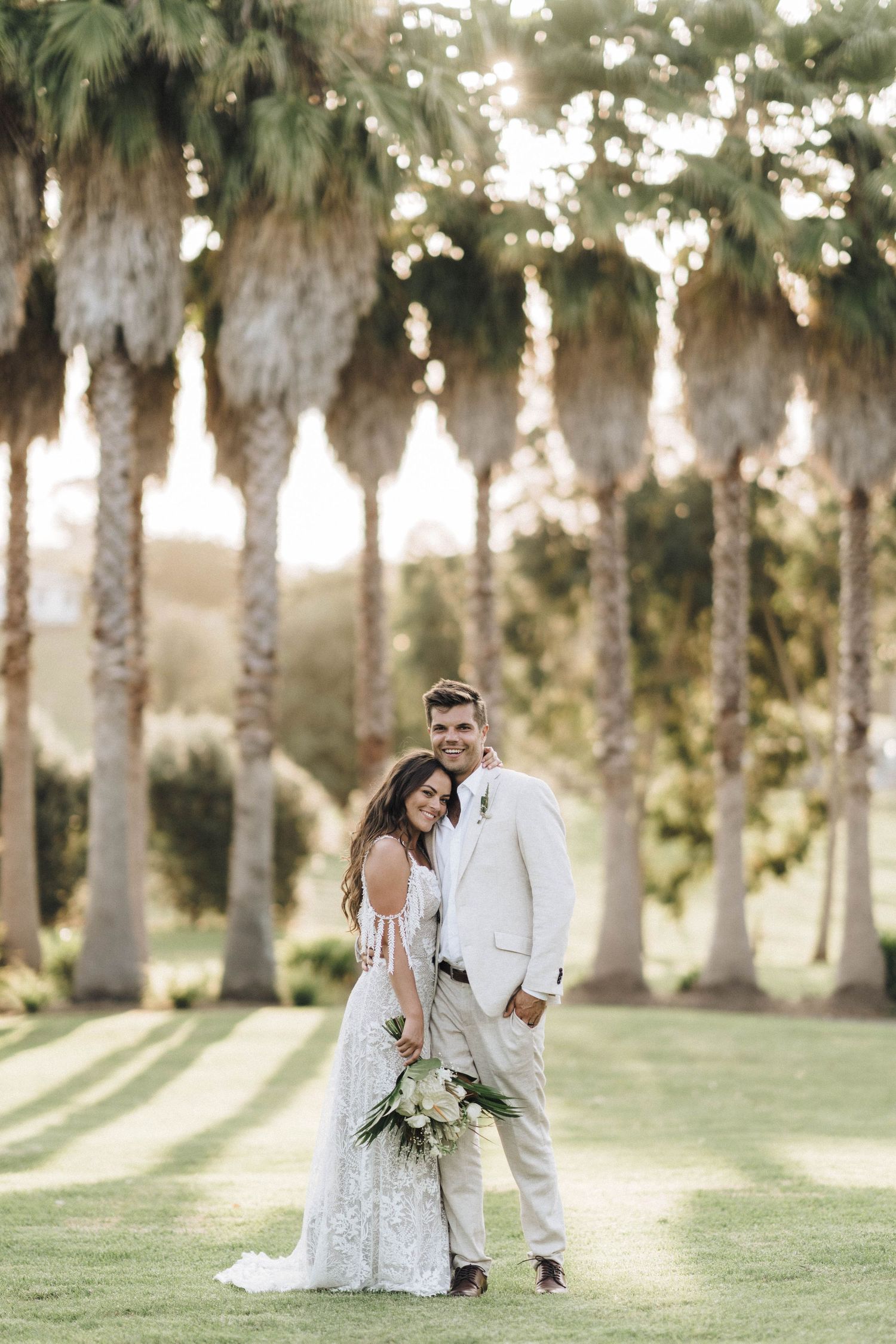 Wedding couple poses for romantic portrait under palm trees at golden hour.
