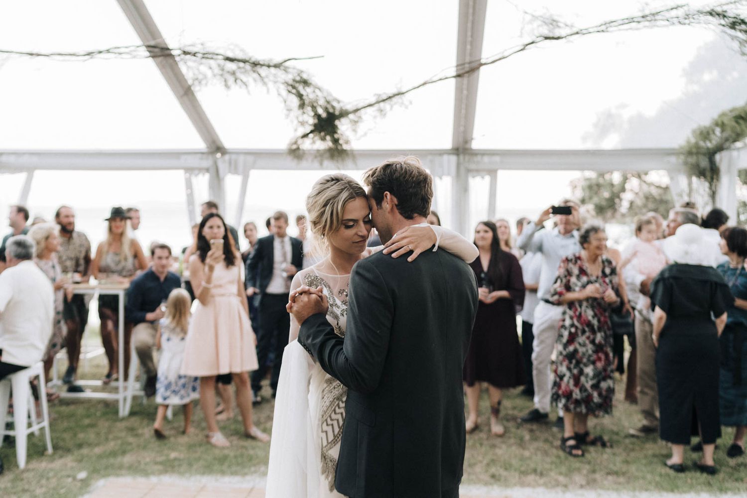 A couple exchanging wedding vows under a white tent during an intimate outdoor ceremony with guests seated nearby.