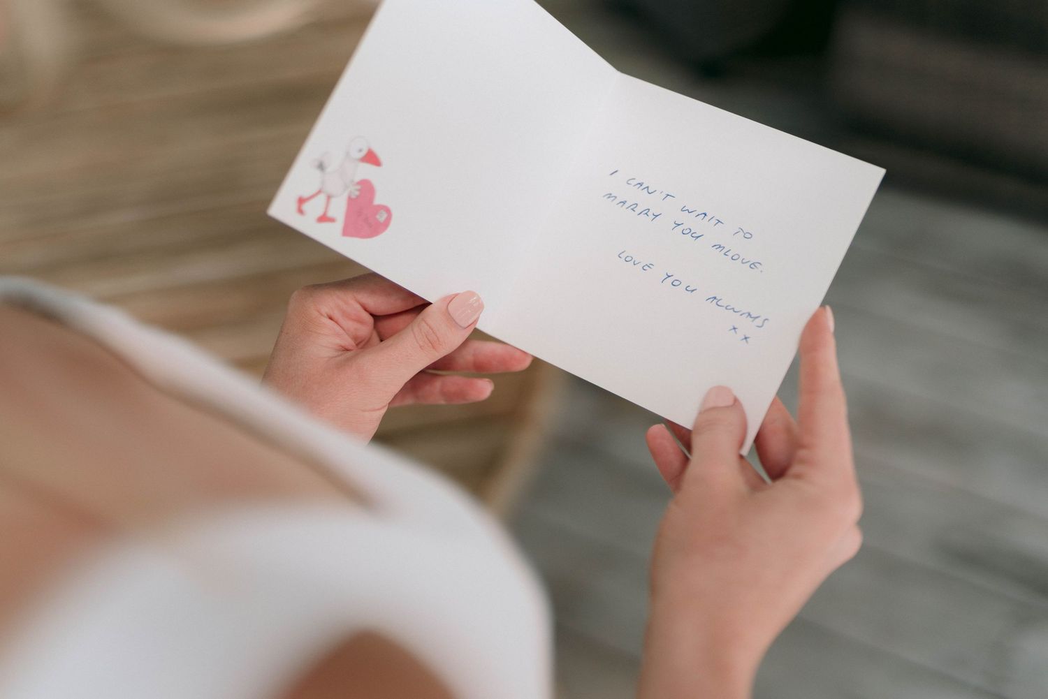 Hands holding a white wedding card or invitation with a pink heart detail.