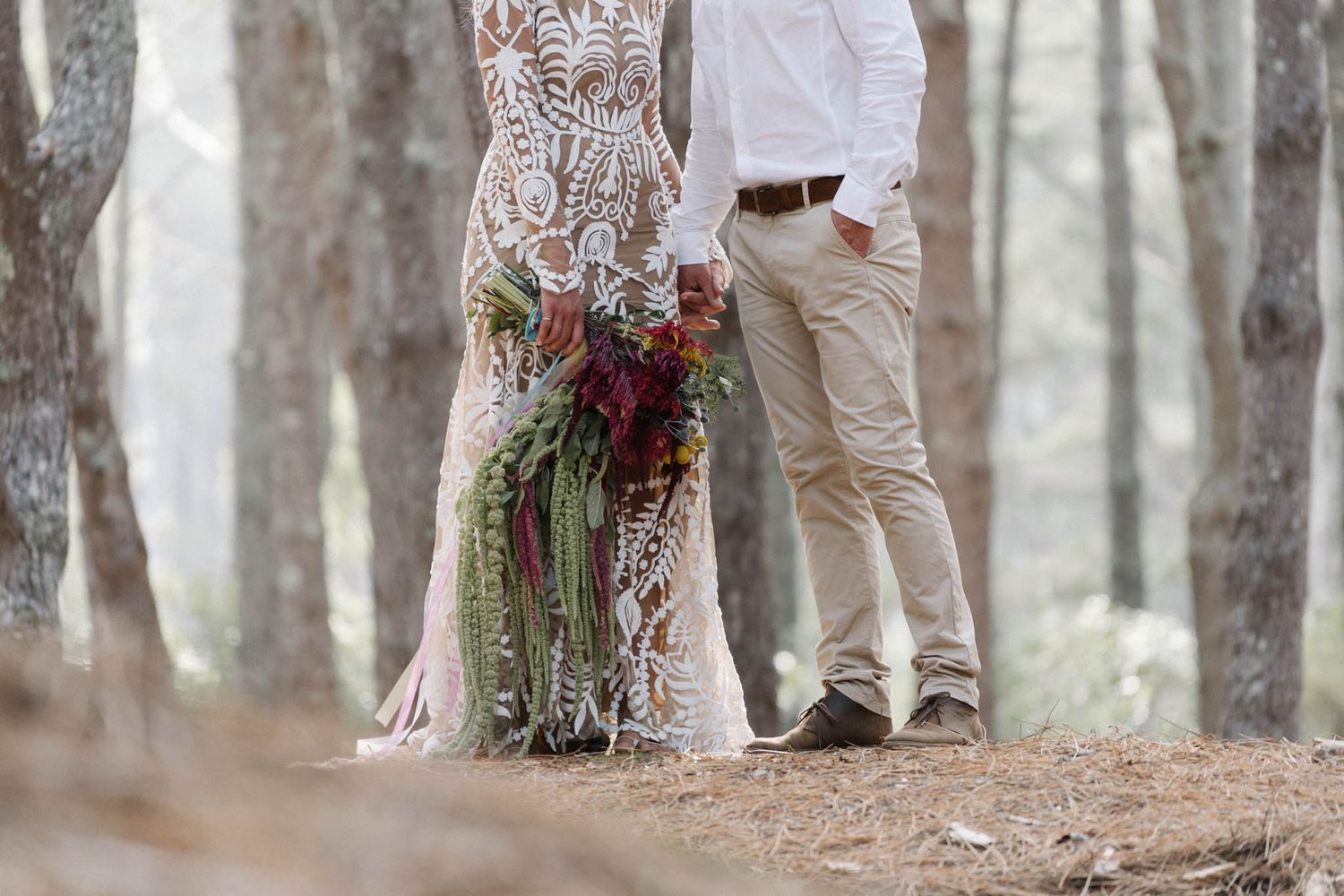 The side profile of a couple embracing in a romantic forest setting with dried flower bouquet details.