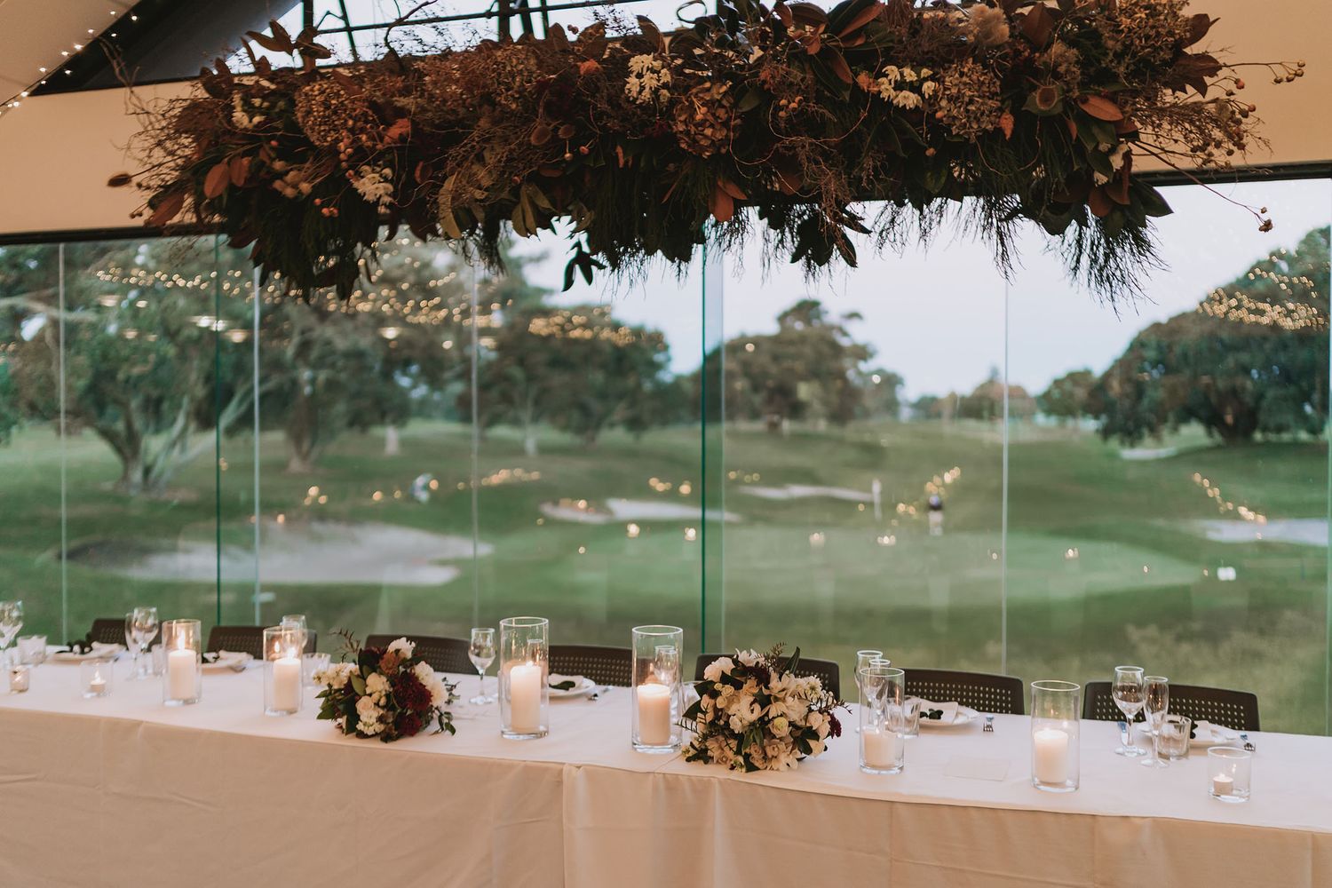 Elegant banquet table setting with floral centerpieces overlooking a scenic golf course through large glass windows.
