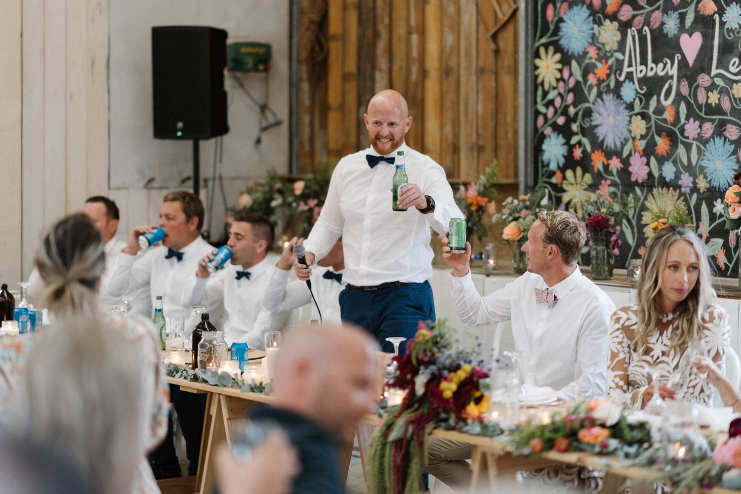 Wedding reception celebration with a toast speech being given at an elegant rustic-themed venue with floral decorations.